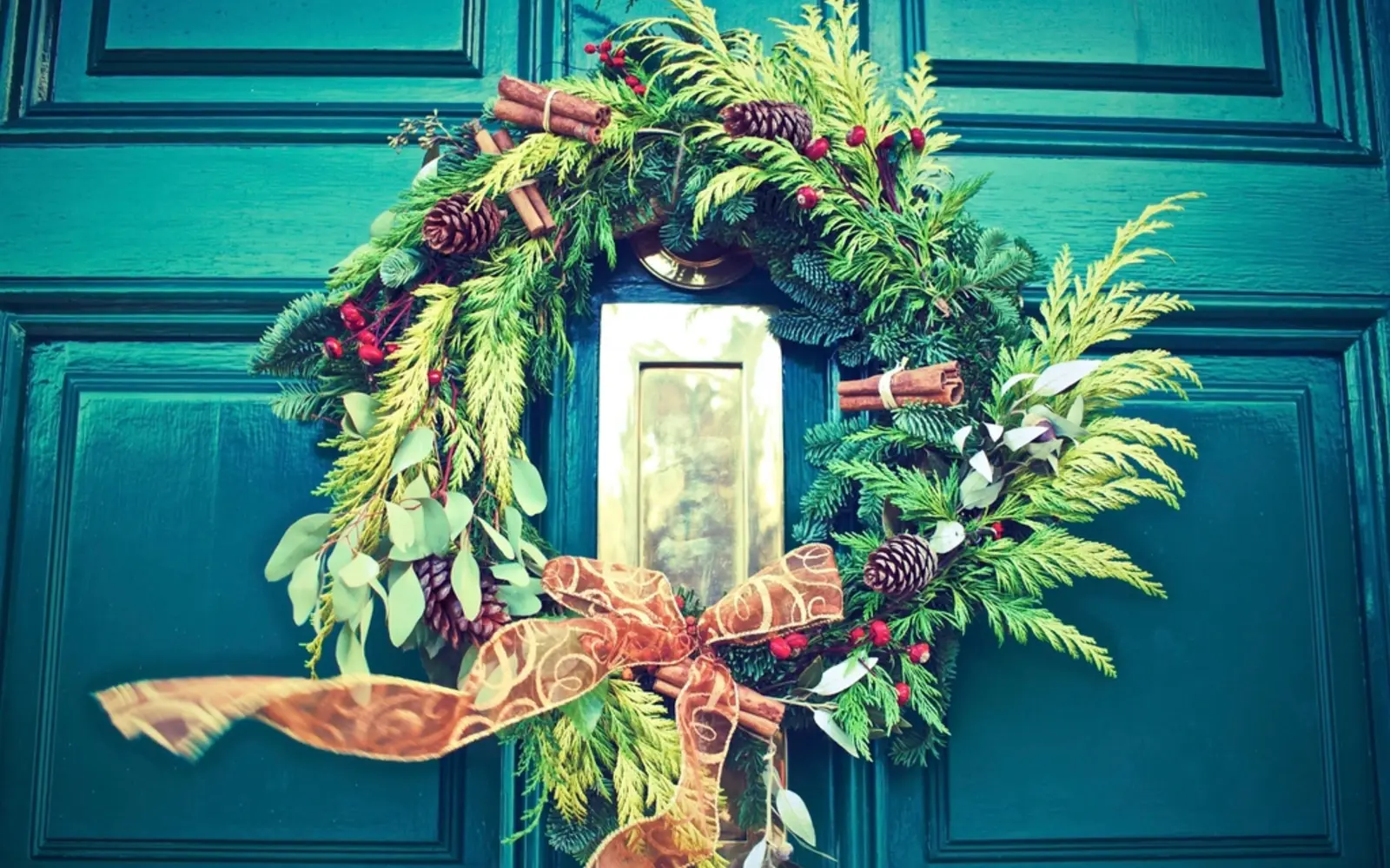 Fresh evergreen Christmas wreath with a ribbon bow on a teal front door