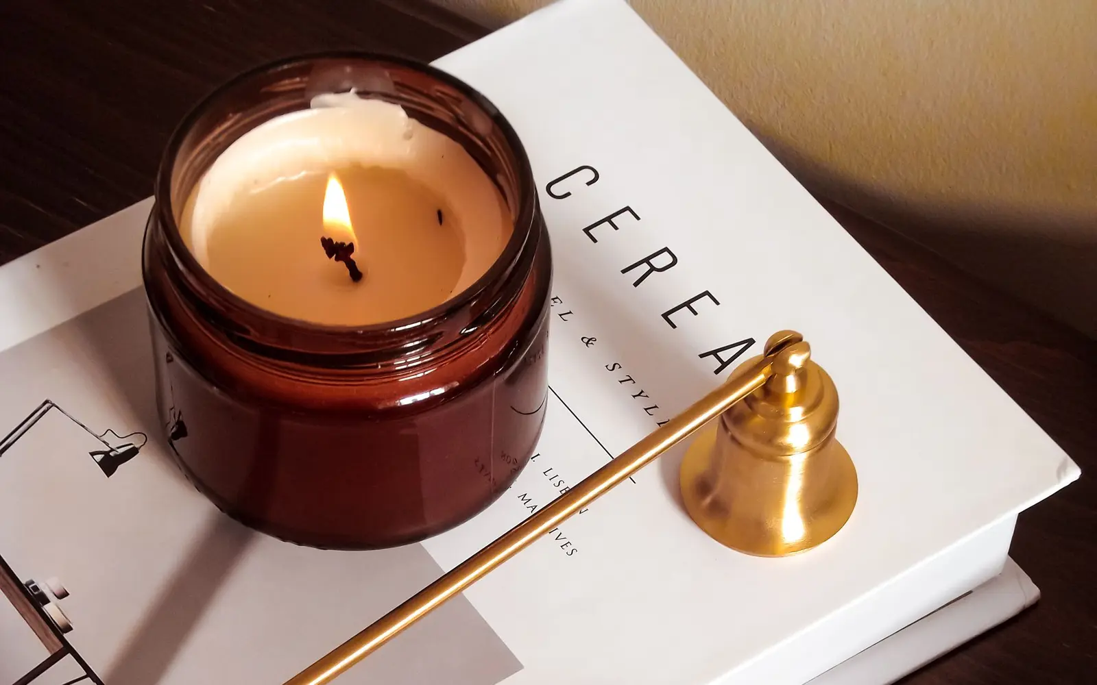 Homemade candle burning in an amber glass jar beside a brass candle snuffer