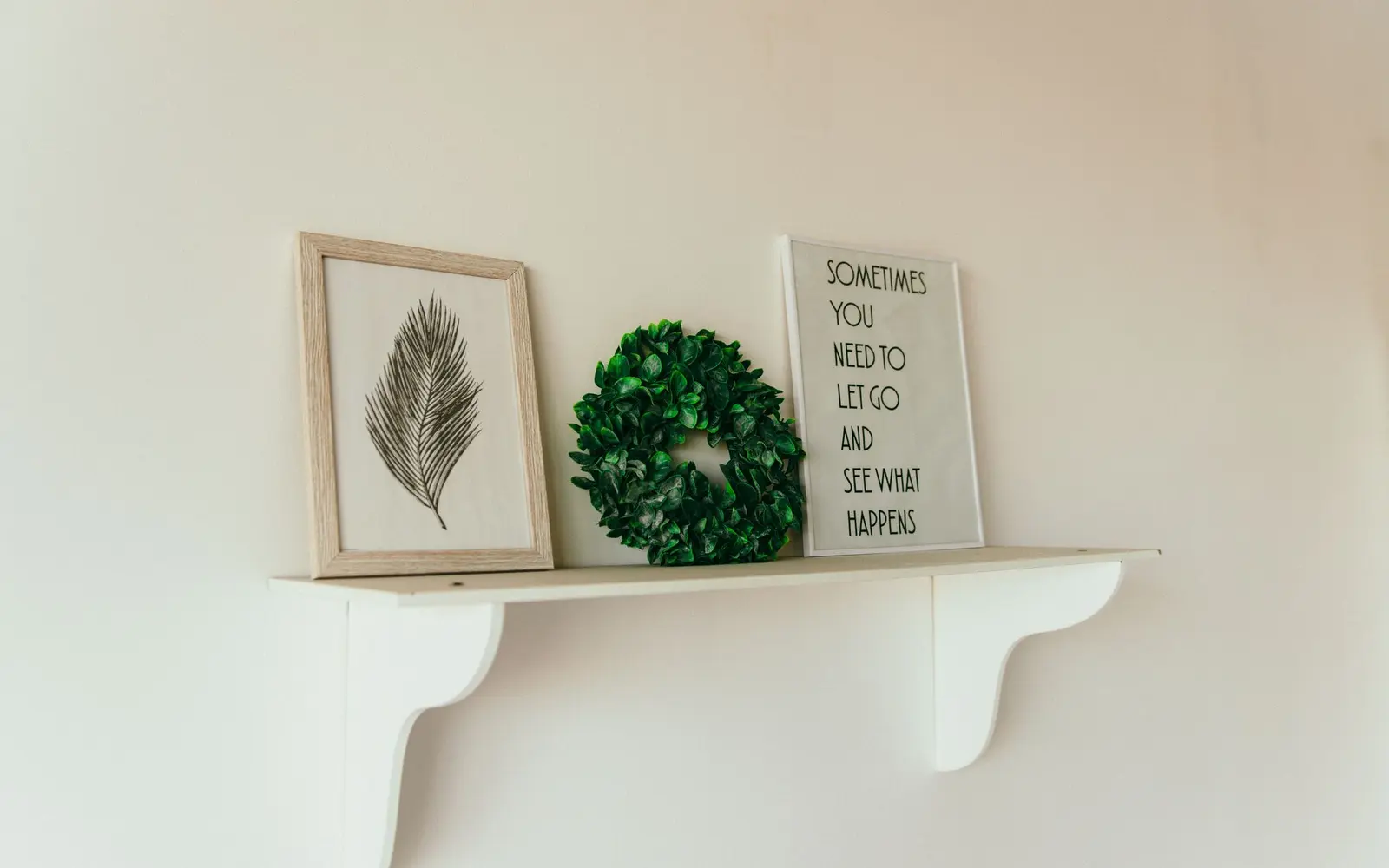 Small green wreath on a white shelf beside framed prints