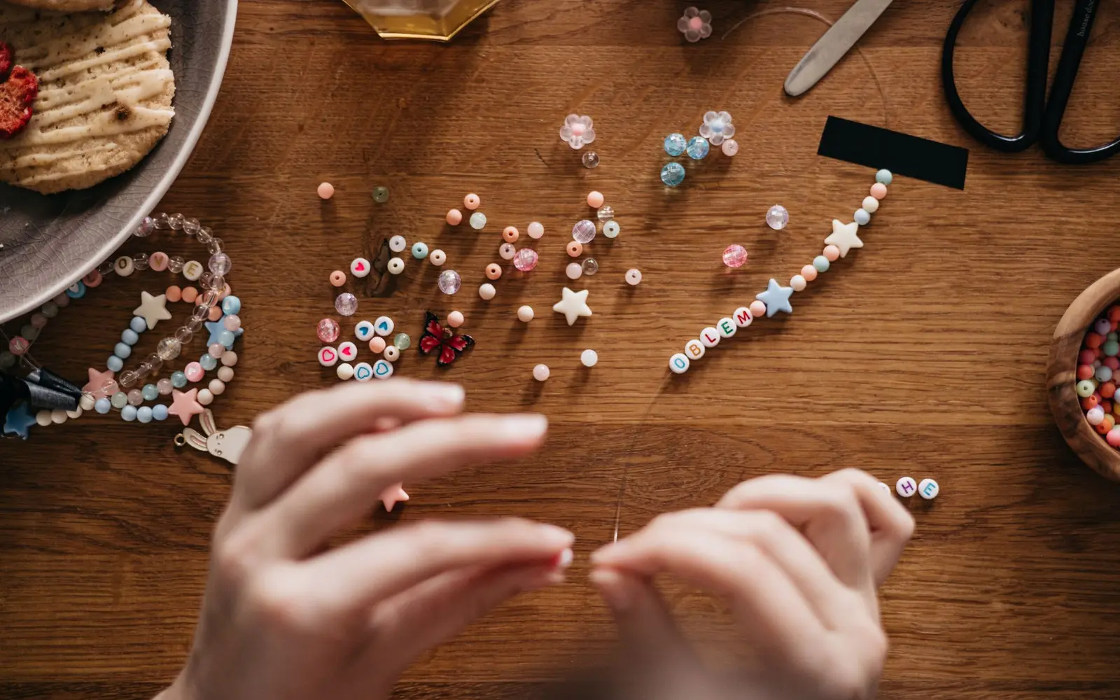Hands stringing beads on a wooden craft table